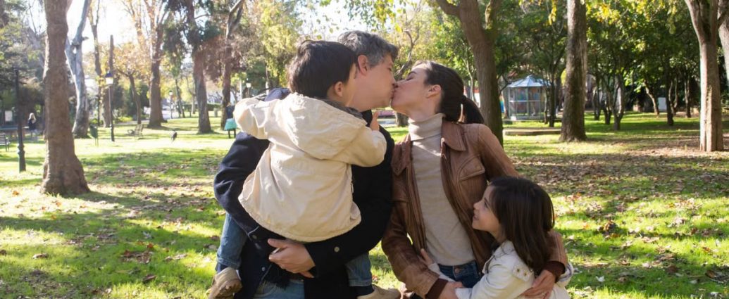 A joyful family sharing a tender moment in a sunny park setting.